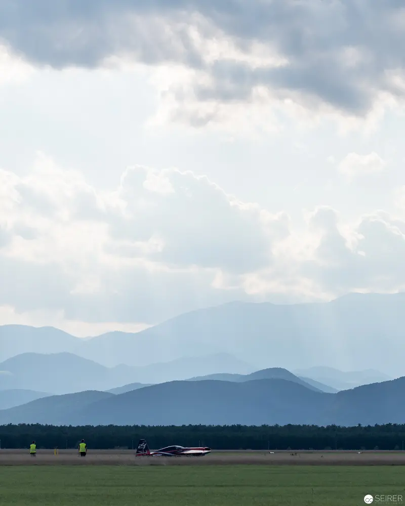 Red Bull Air Race Jet on Verdant Airfield Against Misty Mountain Panorama