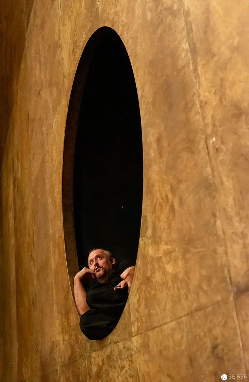 Figure Framed in Oval Aperture Against Textured Amber-Gold Wall