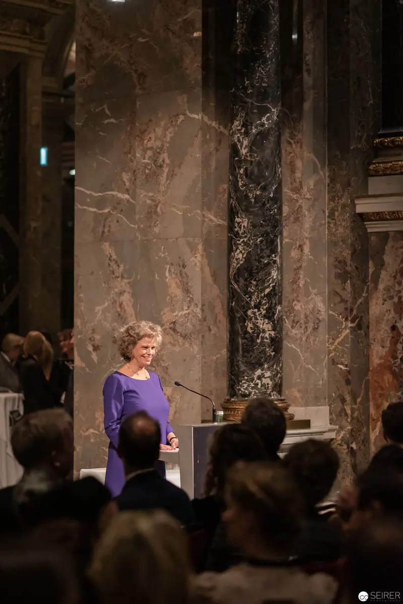 Speaker in Purple Delivering Address at Marble-Clad Venue