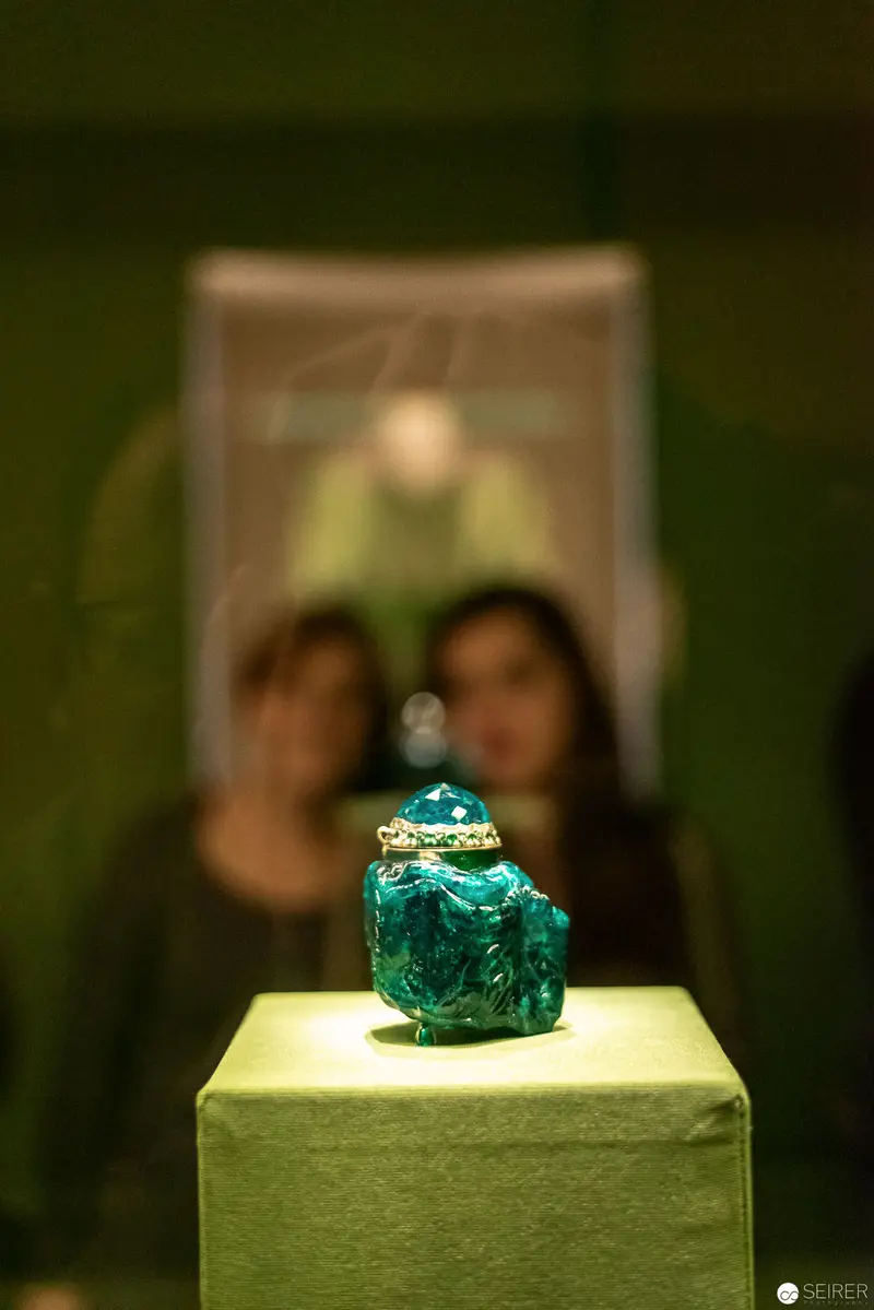 Emerald Gem on Illuminated Pedestal with Blurred Viewers in Background