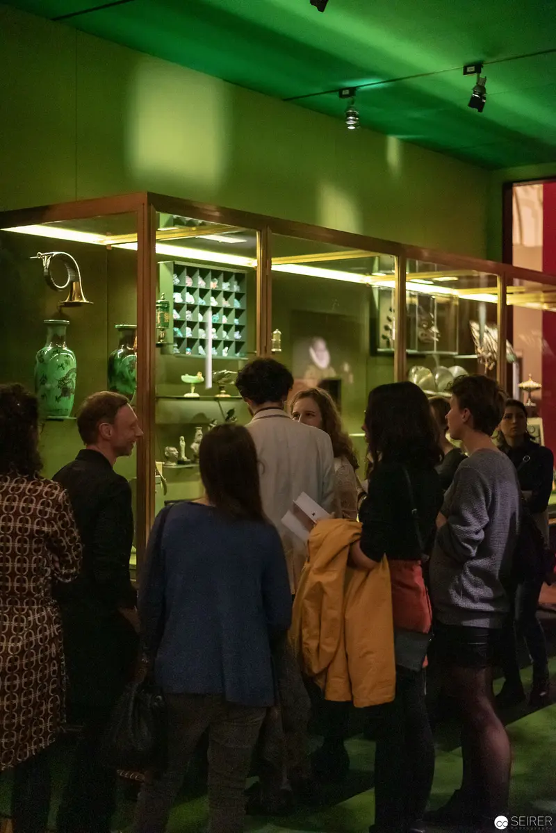 Museum Visitors Examining Curated Exhibit in Green-Tinted Gallery Space