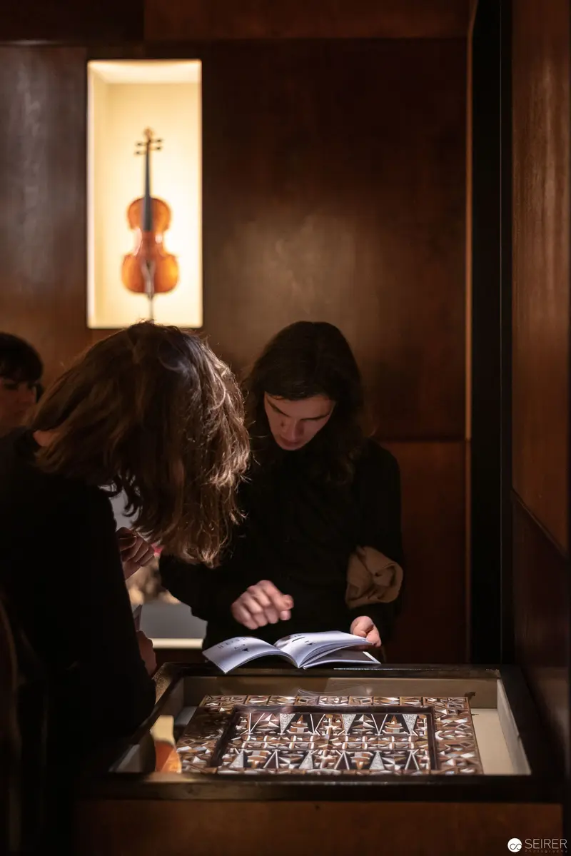 Illuminated Violin Silhouette and Studious Figures in Museum Interior