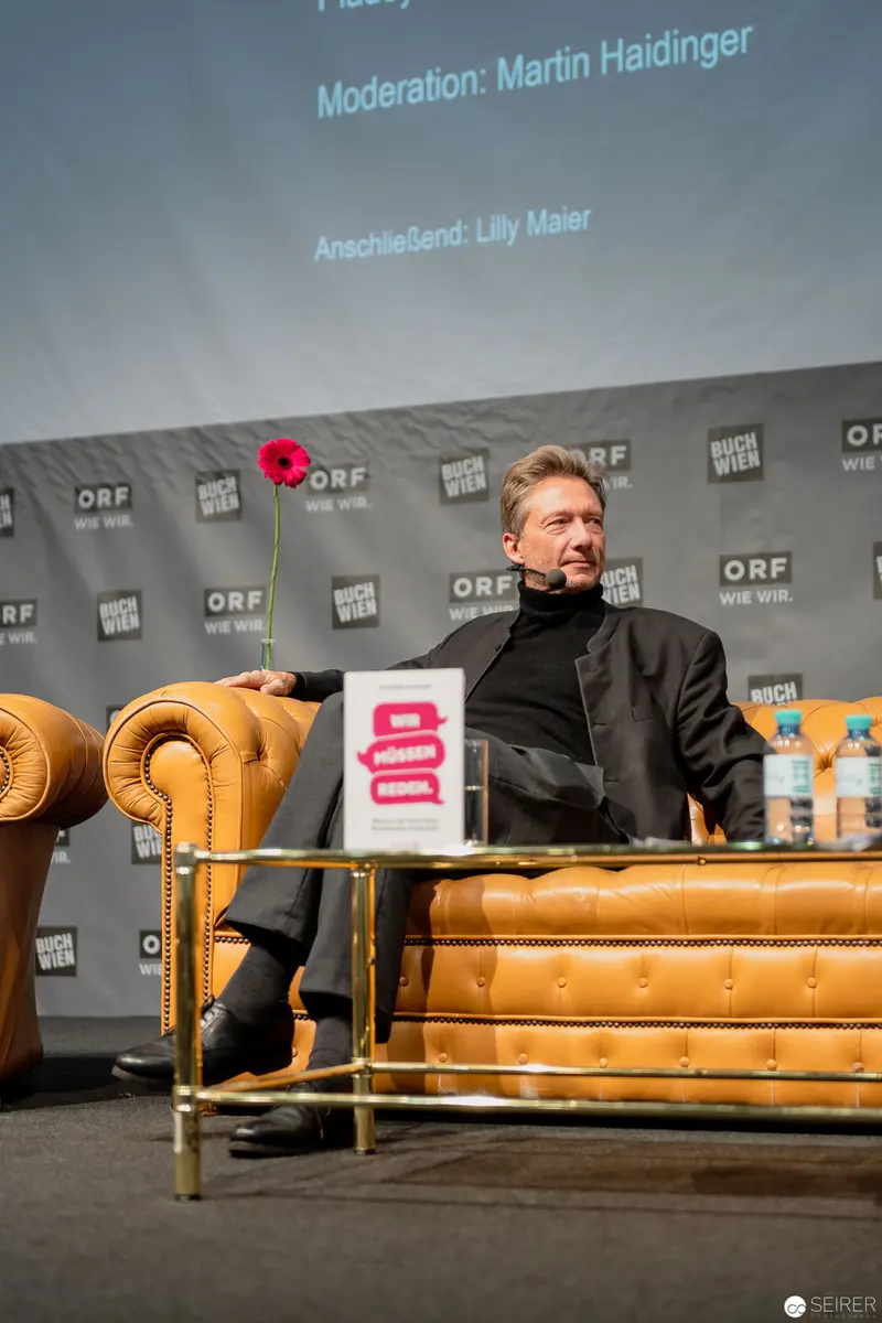 ORF Event Panelist in Leather Armchair with Red Poppy at Press Conference