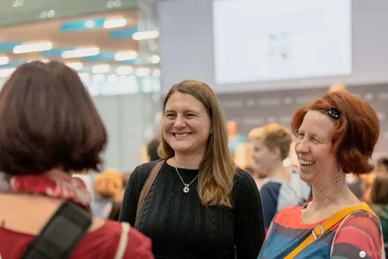 Buch Wien Event: Candid Interaction Between Smiling Colleagues in Conference Space