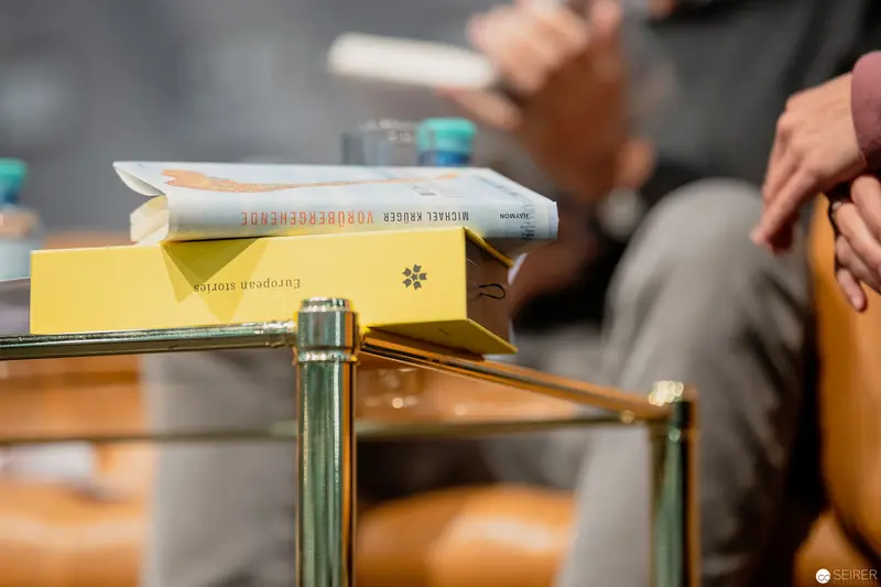 Books and Blurred Figures: Intimate Reading Moment on Glass-Topped Table