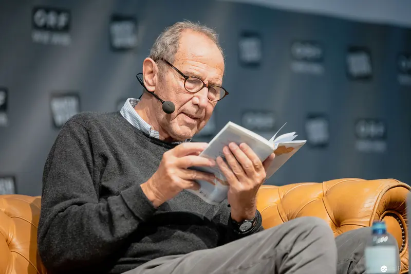 Elderly Scholar Intently Reading Book on Leather Chair at Public Event