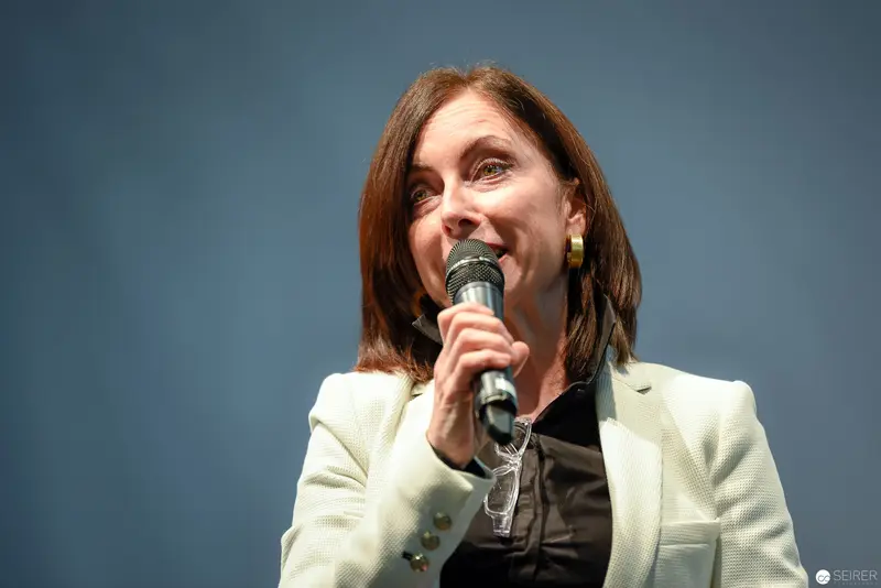Woman in White Blazer Speaking at Podium with Microphone