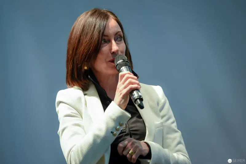 Speaker in White Blazer Addressing Audience with Handheld Microphone