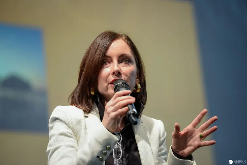 Speaker in White Blazer Addressing Audience with Microphone and Gesture