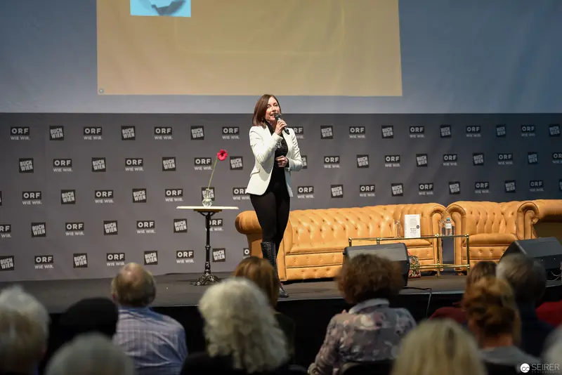 Speaker Presenting at ORF Media Event with Tufted Yellow Sofa Backdrop