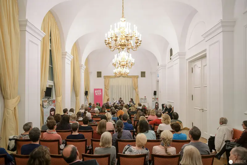 Scholarly Lecture in Ornate White Vaulted Hall with Elegant Chandelier