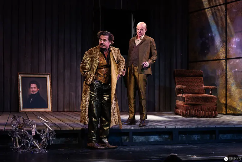 Two Actors on Wooden Stage with Portrait and Atmospheric Scenic Design