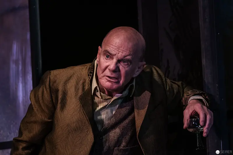 Elderly Actor in Intense Dramatic Pose During Theatrical Performance