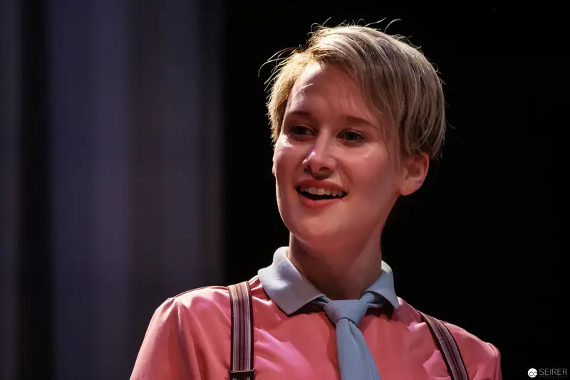 Alexandra Krismer as Lakrimosa in Theatrical Performance with Blue Tie and Pink Shirt
