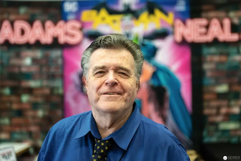 Smiling Man in Blue Shirt at Comic Convention Poster Display