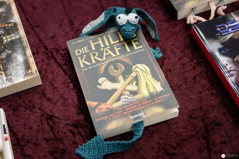 Die Hilfskräfte Book with Teal Knitted Creature on Burgundy Velvet Background