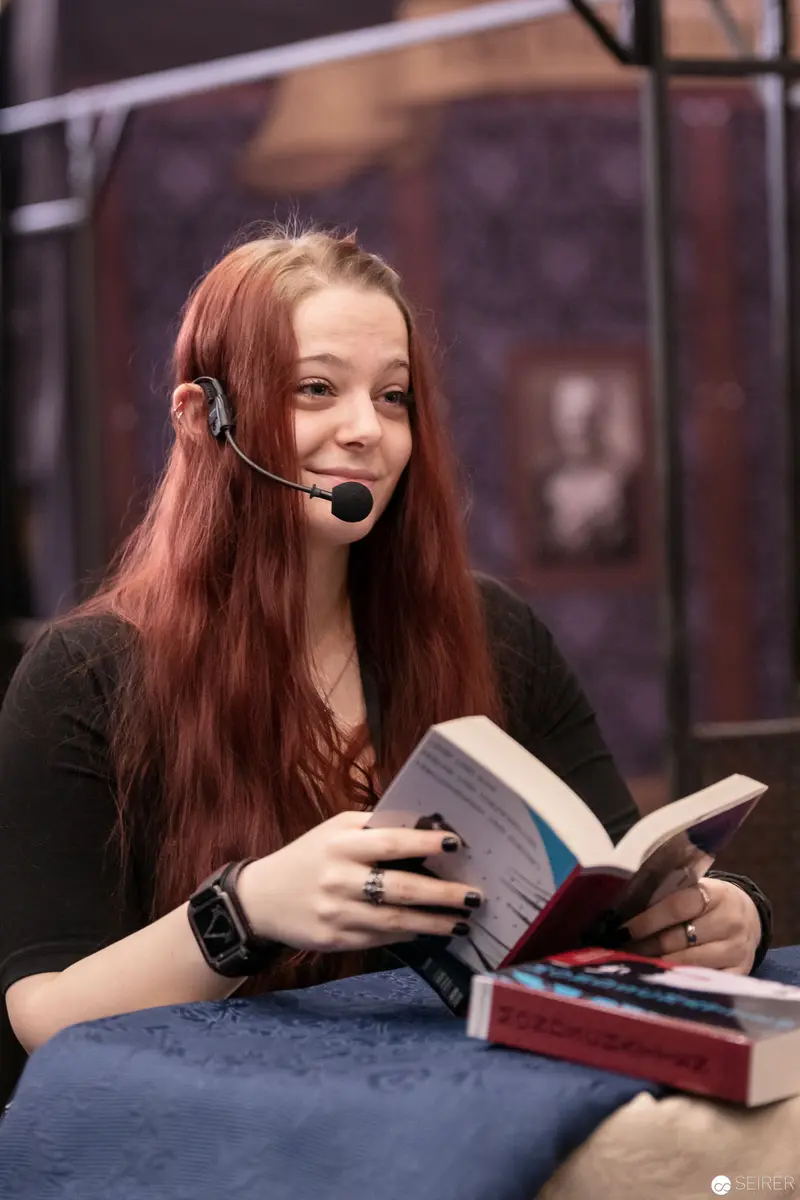 Young Woman in Headset Reading at Vienna ComicCon 2018 Book Display