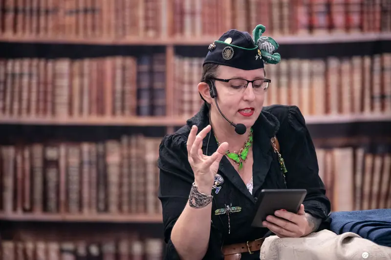 Scholarly Woman in Steampunk Attire Consulting Digital Device at Library