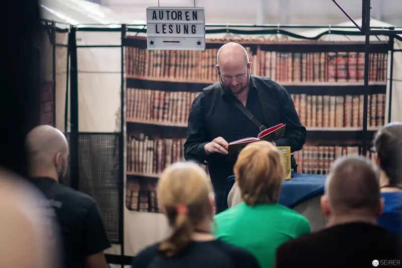Author Reading at Book Exhibition with Attentive Audience Behind Vintage Library Backdrop