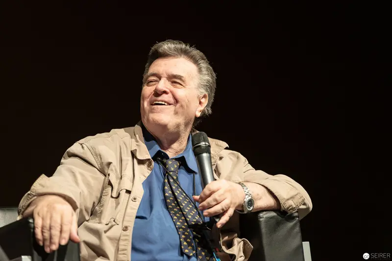 Comedian in Beige Jacket Laughing During Stage Performance with Microphone