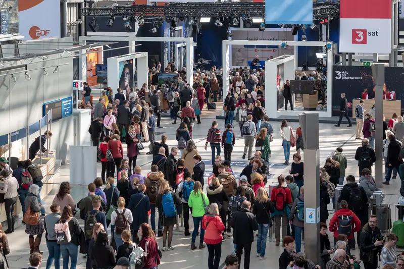 Crowded Exhibition Hall with Visitors Navigating Information Displays and Media Signage