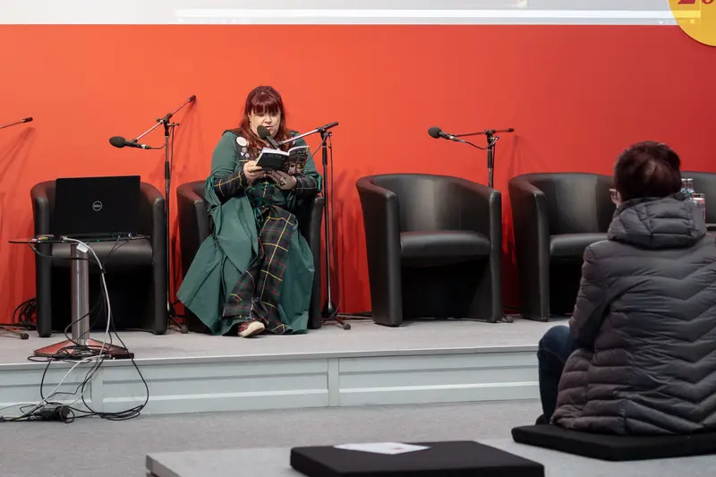 Author Reading at Literary Event Against Vibrant Orange-Red Background