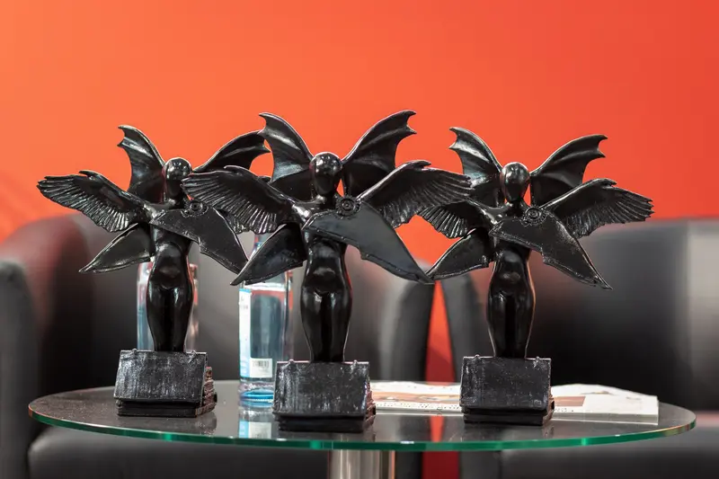 Black Winged Figurines on Glass Table Against Vibrant Orange Background