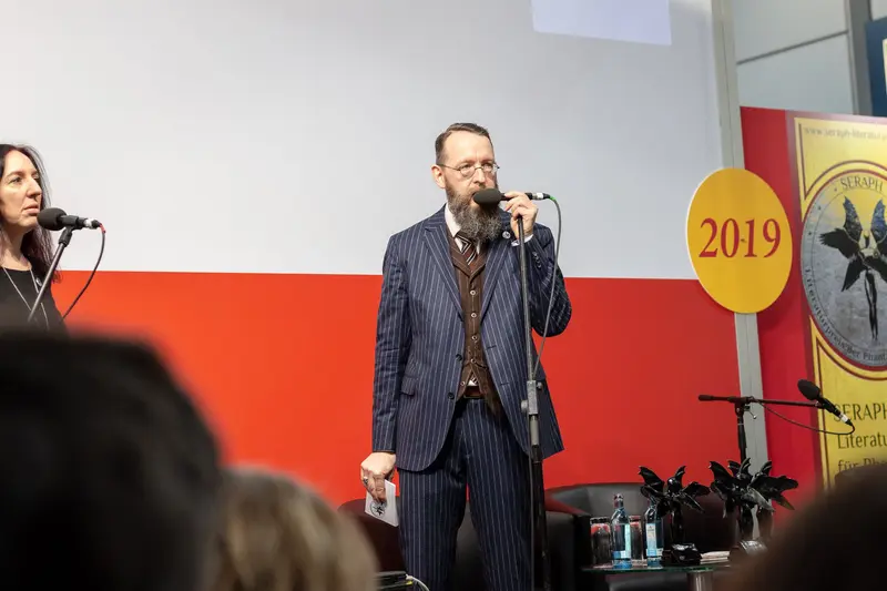 Speaker in Pinstripe Suit Addresses Literary Event During 2019 Conference