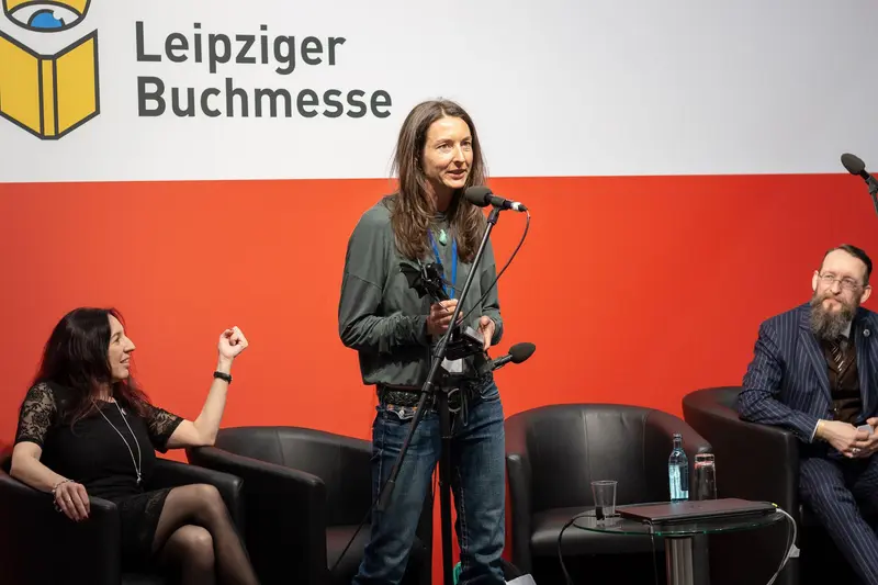 Leipziger Buchmesse Panel Discussion with Standing Speaker and Gesturing Participants