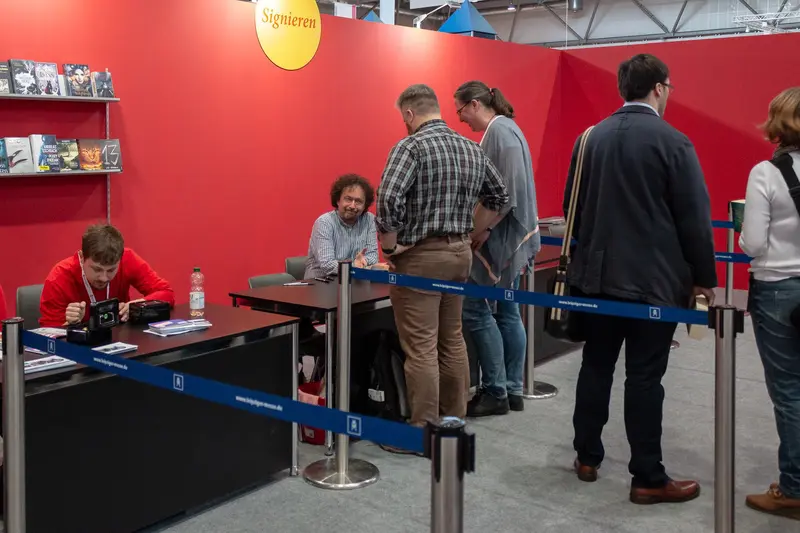 Book Signing Event with Seated Authors at Cultural Exhibition Behind Crowd Barriers