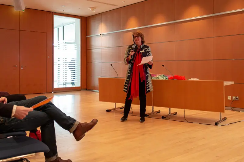 Presenter in Patterned Coat Lecturing in Minimalist Wood-Paneled Conference Room