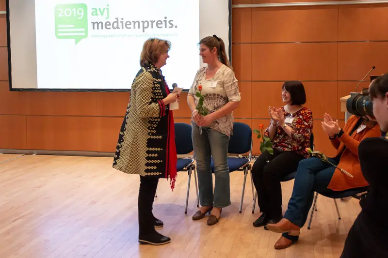AVI Medienpreis Award Ceremony: Two Women Interact on Wooden Stage