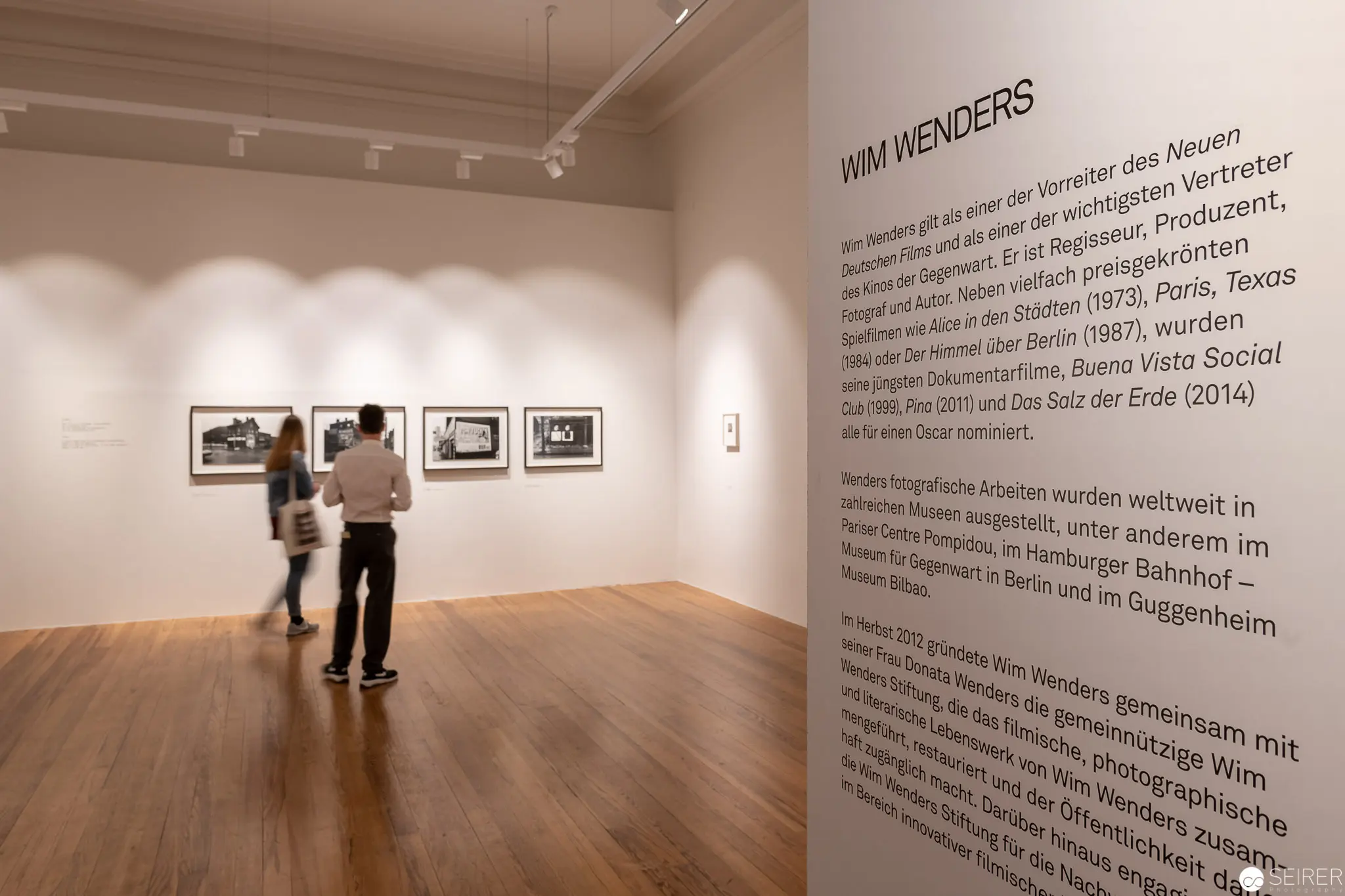 Wim Wenders Exhibition Interior with Gallery Visitors Examining Photographic Prints