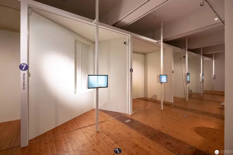 Minimalist Gallery Installation with Suspended Digital Displays and Wooden Flooring