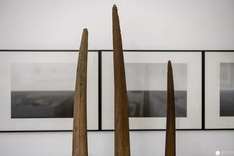 Three Tapered Wooden Spikes Against Minimalist Gallery Wall Backdrop