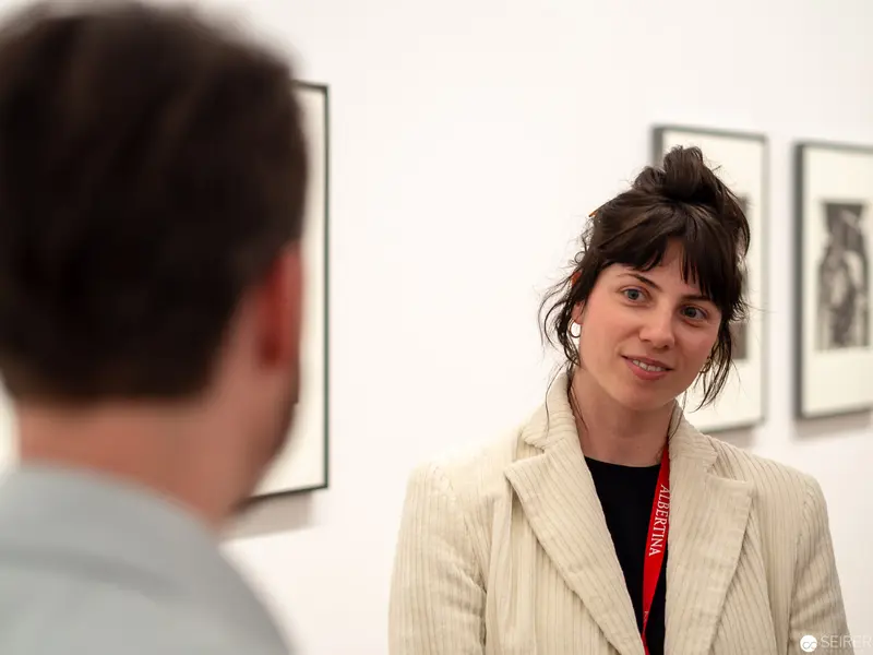 Gallery Dialogue: Curator in Cream Blazer amid Framed Photographic Exhibits