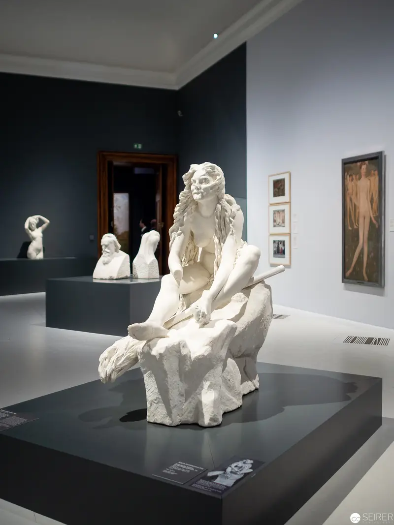 White Marble Sculpture of Seated Female Figure in Museum Gallery Setting