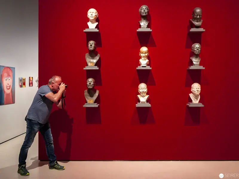 Museum Visitor Examining Sculptural Bust Installation on Crimson Wall