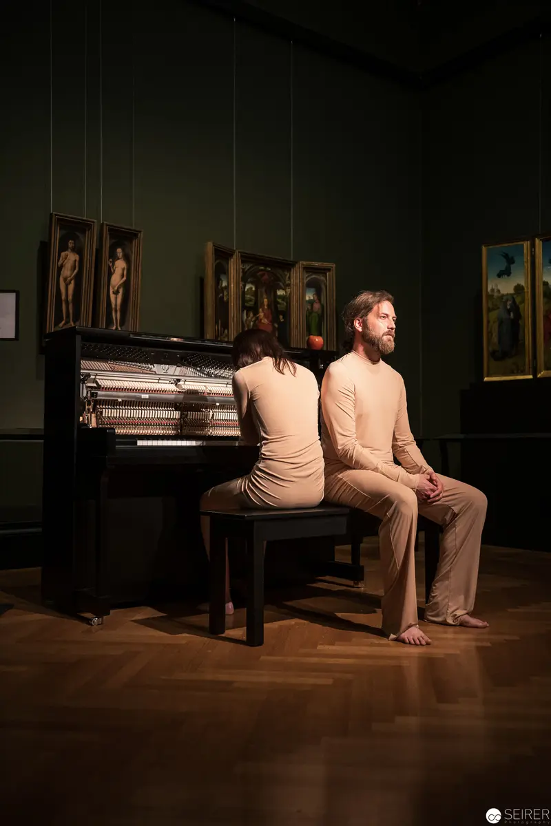 Ganymed In Love: Two Figures Seated by Piano in Intimate Museum Setting