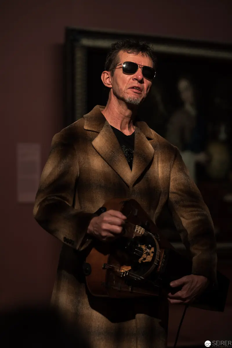 Contemplative Figure in Vintage Coat with Sunglasses at Museum Exhibition