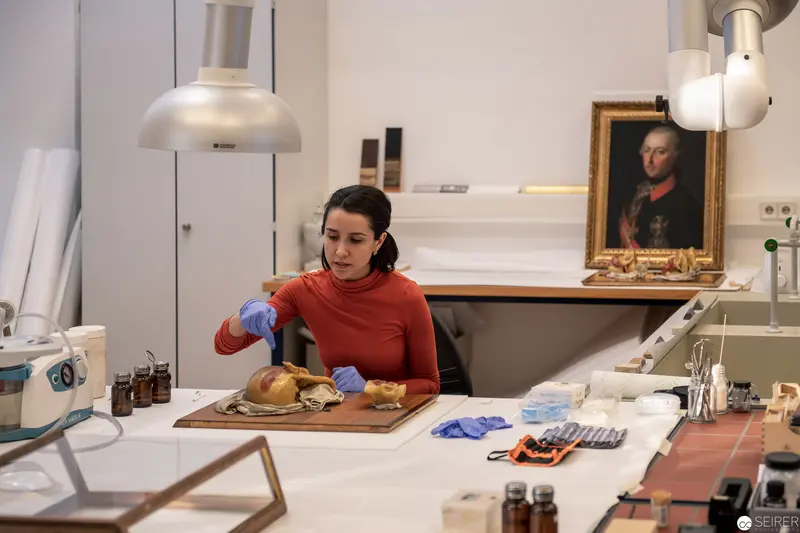 Art Conservator in Red Sweater Examining Historical Artifact Under Laboratory Lighting
