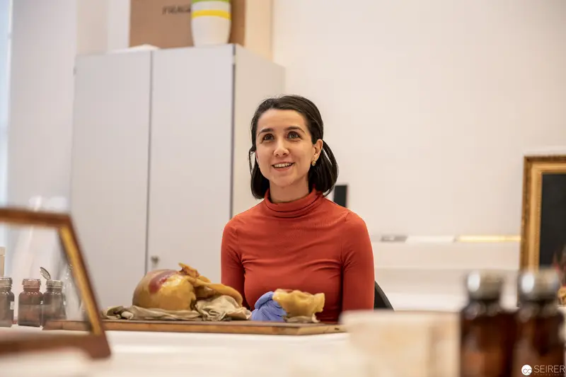 Conservation Specialist in Red Sweater Examining Archaeological Artifacts at Workstation