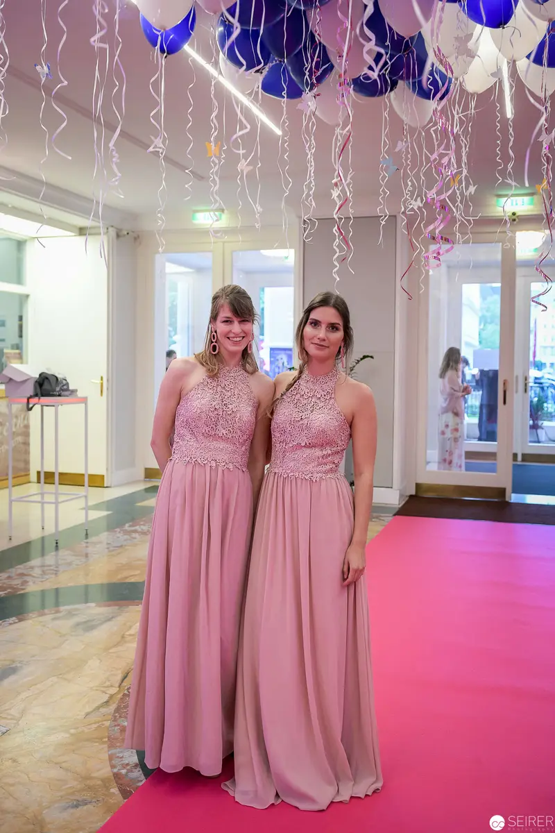 Two Women in Blush Pink Gowns Beneath Blue and White Balloons