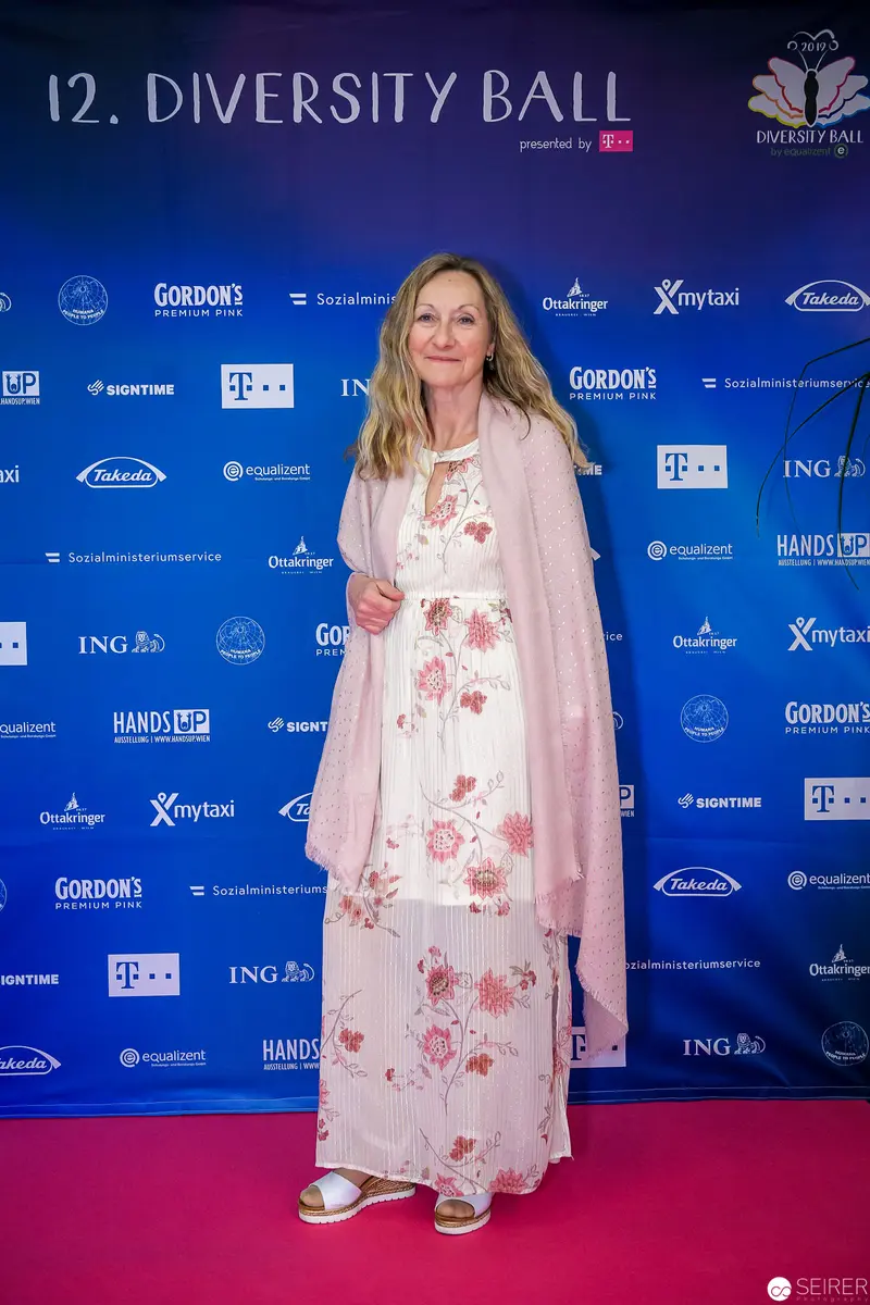 Woman in Floral Dress at 12th Diversity Ball Sponsor Backdrop