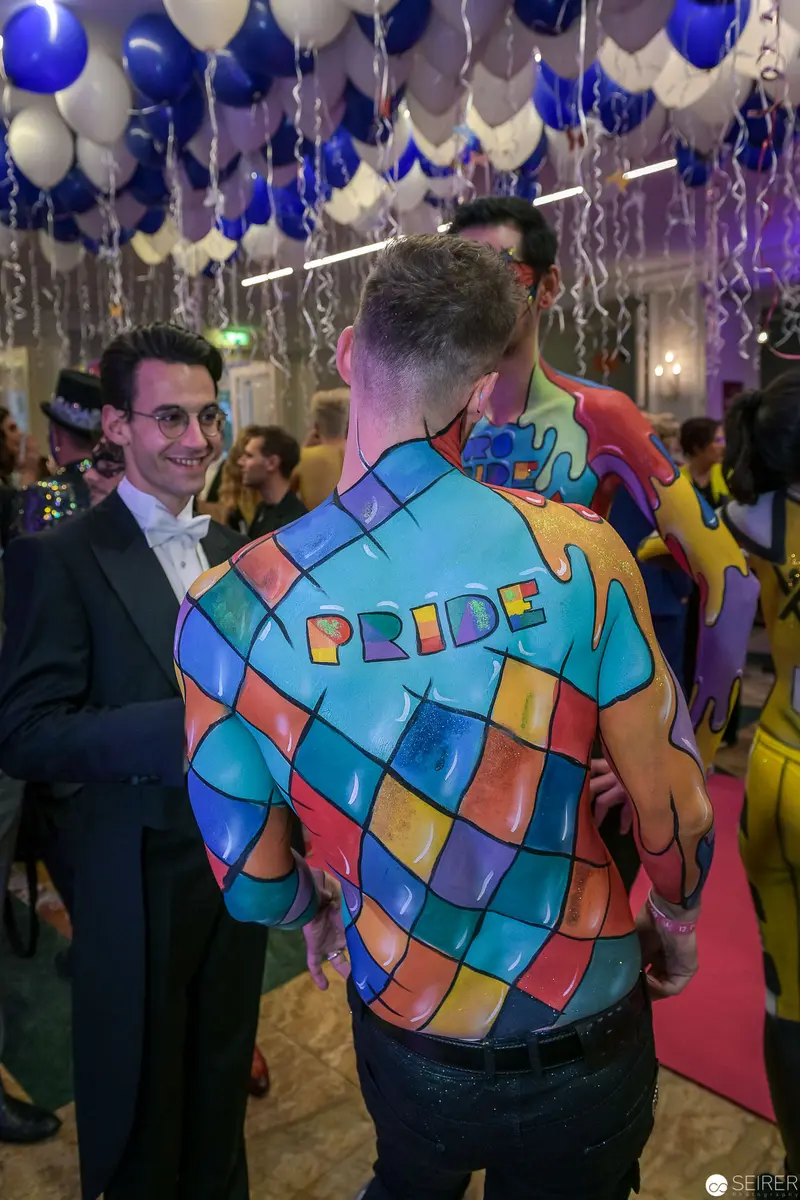 Pride Event Attendee in Colorful Geometric-Patterned Jacket Amid Balloon Decor