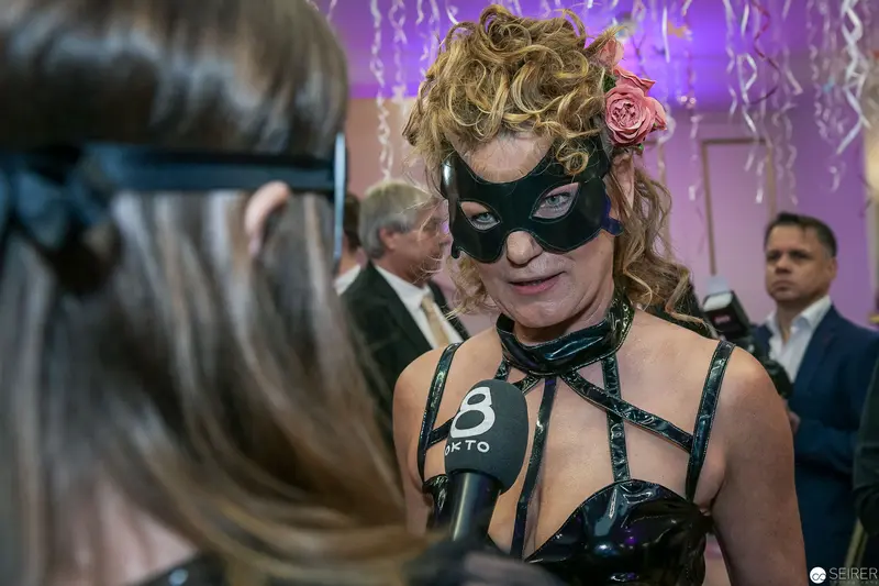 Masked Woman in Dramatic Costume Gives Television Interview at Stylized Event