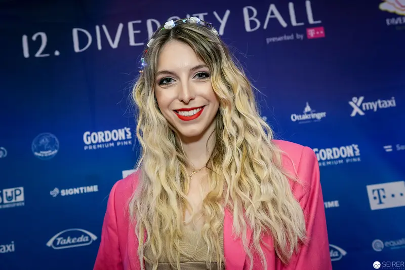 12th Diversity Ball Attendee in Vibrant Pink Blazer and Wavy Blonde Hair