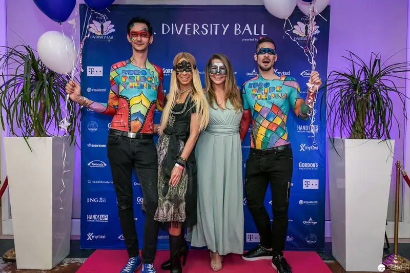 Diversity Ball 2024: Four Guests in Vibrant Costumes Pose on Pink Carpet