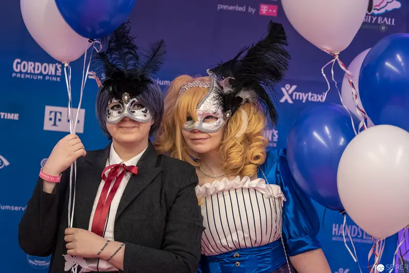 Two Masked Performers at Masquerade Event with Blue and White Balloons