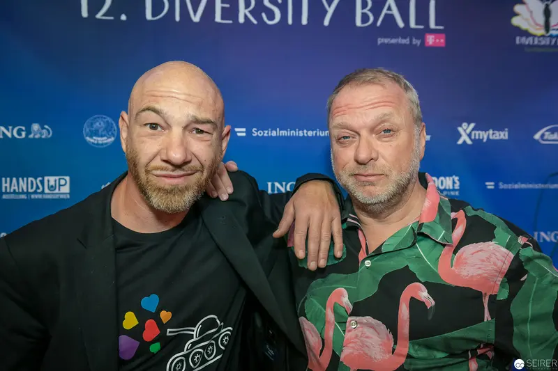 Two Men at 12th Diversity Ball, Posing with Colorful Flamingo and Heart Motifs